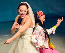 Photo of Jasmin Wagner performing in Tussipark. She is in a wedding dress, eyeliner streaked down her face, singing into a hairbrush as if it were a microphone. Another actress is playing an air guitar and leaning her back against Wagner's.